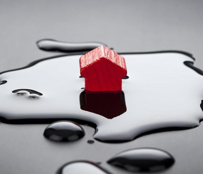 A little red wooden house placed in the center of a puddle on top of a dark grey surface